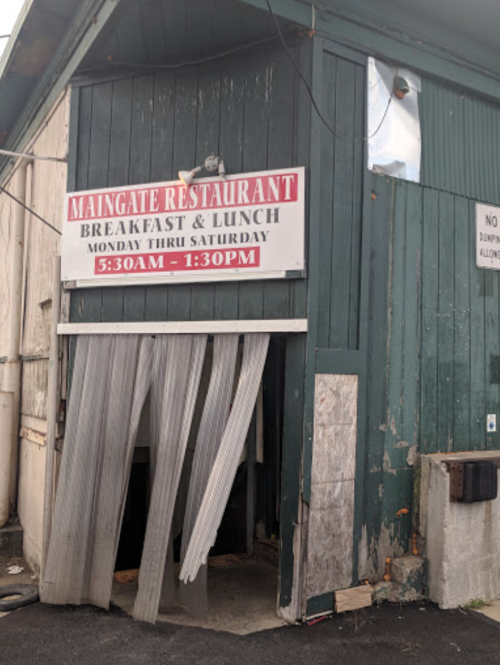 Exterior of Maingate Restaurant with a sign for breakfast and lunch hours, featuring a partially open entrance.