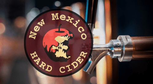 Logo of New Mexico Hard Cider featuring an apple and skull design, with a tap in the background.
