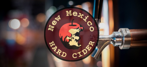 Logo of New Mexico Hard Cider featuring an apple and the text "New Mexico Hard Cider" on a blurred background.