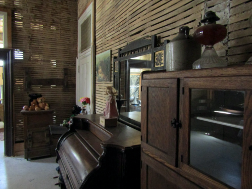 A vintage room with wooden walls, an antique piano, and various decorative items on shelves and furniture.
