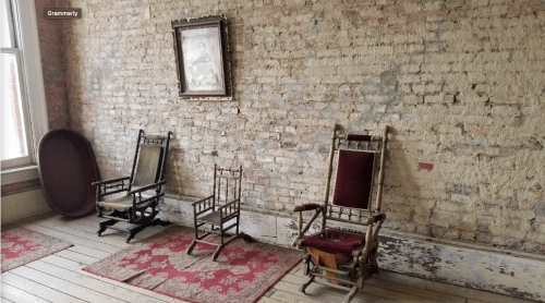 Two vintage rocking chairs on a wooden floor, set against a brick wall with a framed picture above.