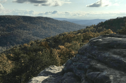 A scenic view of rolling hills and valleys, with autumn foliage and a rocky foreground under a cloudy sky.