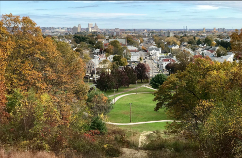 A scenic view of a town with autumn foliage, featuring parks and buildings in the distance under a clear sky.