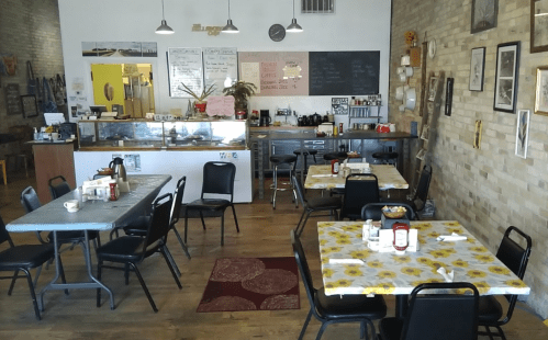 Cozy café interior with tables covered in floral tablecloths, a counter with a display case, and a warm, inviting atmosphere.