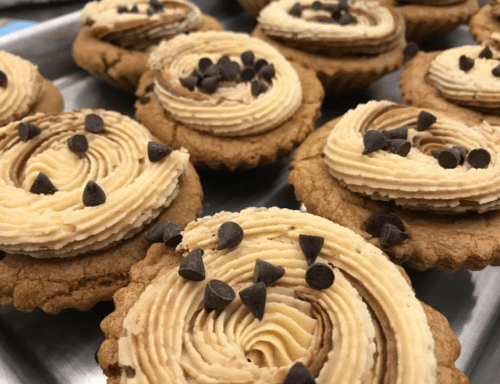 Close-up of freshly baked cupcakes with swirled frosting and chocolate chips on top, arranged on a tray.