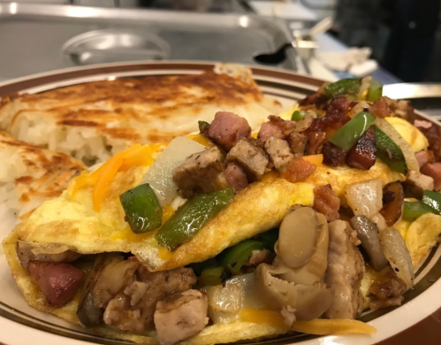A hearty omelette filled with vegetables, meats, and cheese, served with crispy hash browns on the side.