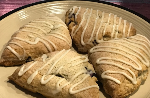 Four freshly baked scones drizzled with white icing, arranged on a round plate.