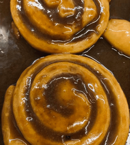 Close-up of two freshly baked cinnamon rolls drizzled with sticky caramel sauce.