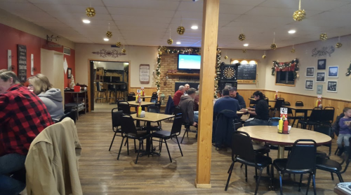 A cozy restaurant interior with wooden floors, tables, and festive decorations. Patrons are enjoying their meals.