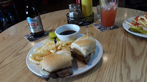 A plate with two sliders, crinkle fries, a dipping sauce, and a drink on a table in a casual dining setting.