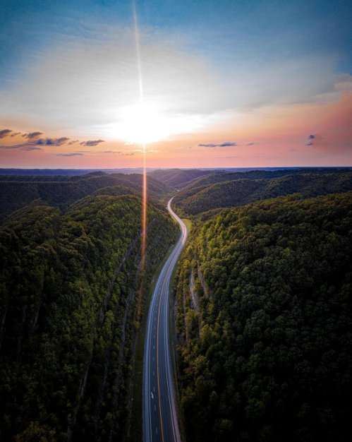 A winding road through lush green hills under a colorful sunset sky.