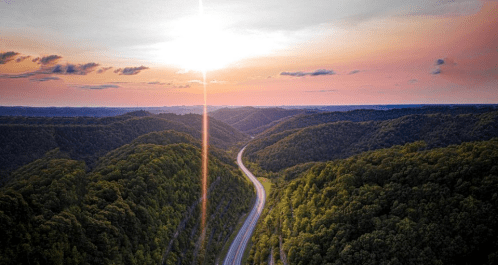 A winding road through lush green hills under a colorful sunset sky.