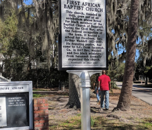 Sign for the First African Baptist Church, detailing its history and founding, with a person walking in the background.
