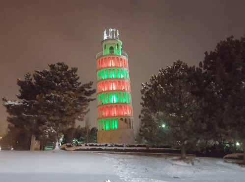 A snow-covered tower illuminated in red and green lights at night, surrounded by trees.