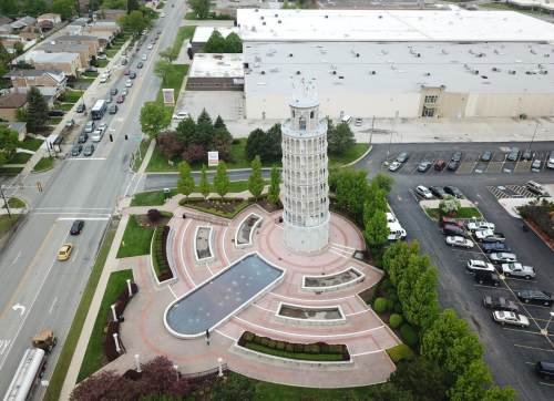 Aerial view of a tower-like structure surrounded by landscaped gardens and a parking lot.