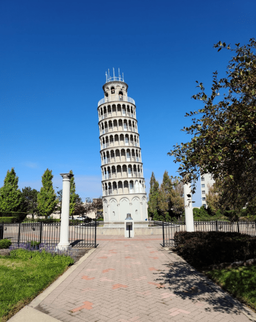 A leaning tower surrounded by greenery and a clear blue sky, with a pathway leading up to it.