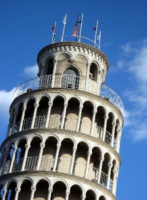 A close-up view of a tall, ornate tower with multiple arches and flags against a blue sky.
