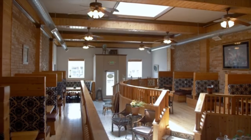 Interior of a cozy restaurant featuring wooden decor, booths, and large windows for natural light.