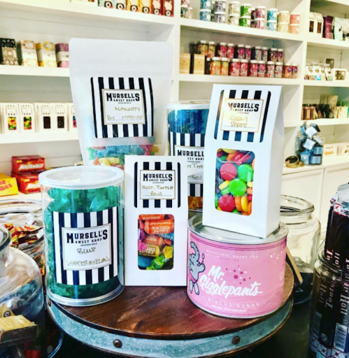 A display of colorful candy jars and bags on a wooden table in a shop, featuring various sweet treats.