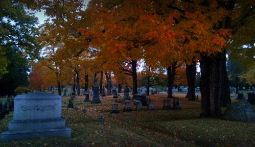 A serene cemetery scene with vibrant autumn trees and gravestones, creating a peaceful, reflective atmosphere.