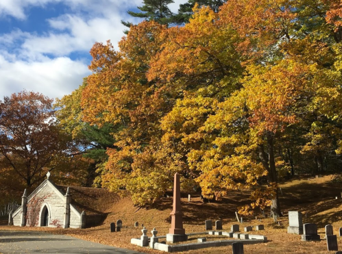 A serene cemetery scene with colorful autumn trees and a stone mausoleum under a blue sky.