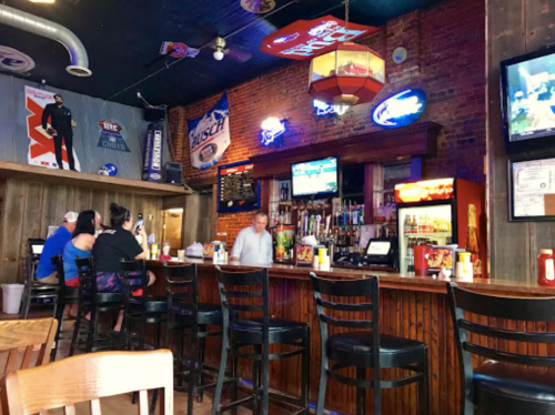 A cozy bar interior with wooden accents, patrons at the counter, and various beer signs and TVs on the walls.