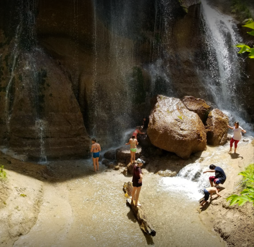 People enjoying a sunny day near a waterfall, playing in the water and exploring the rocky surroundings.