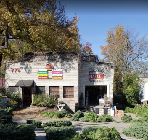 A quaint market building surrounded by greenery, featuring signs for fresh, local produce and goods.