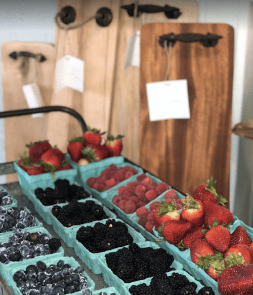 A display of fresh berries in baskets, including strawberries, raspberries, blackberries, and blueberries, with wooden boards in the background.