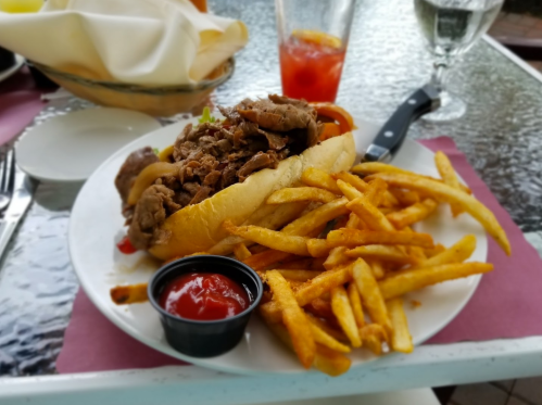 A plate featuring a sandwich filled with meat, served with a side of fries and a small cup of ketchup.