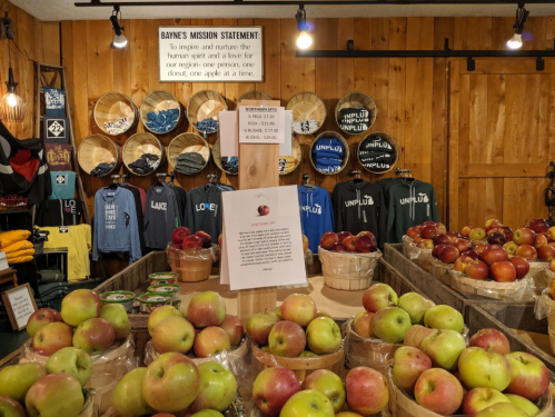 A display of apples in baskets with a sign about Bayne's mission statement and clothing hanging on the wall behind.