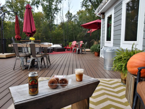 A cozy outdoor deck with seating, a drink, and snacks, surrounded by trees and colorful umbrellas.