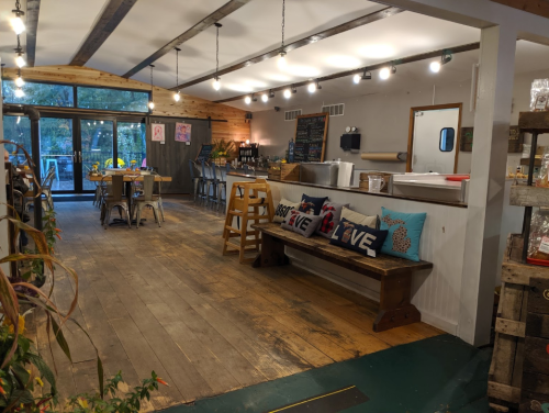 A cozy, modern café interior with wooden floors, seating, and a counter, featuring bright lights and decorative pillows.