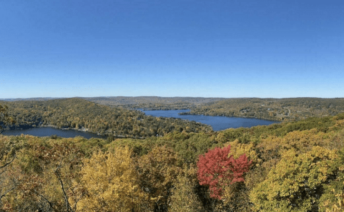 A panoramic view of a colorful autumn landscape with lakes and rolling hills under a clear blue sky.