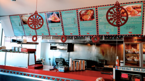 Colorful menu boards hang above a red counter in a festive restaurant, decorated with wreaths and holiday ornaments.