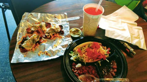 A table with a plate of tacos, beans, and nachos, alongside a drink and napkins.
