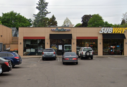 A parking lot with cars in front of a building featuring a restaurant sign and a Subway logo on the right.