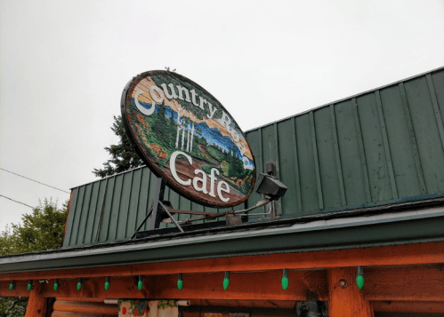 Sign for "Country Moon Cafe" featuring a scenic design, mounted on a green building under a cloudy sky.