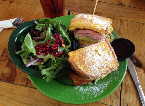 A plate with a sandwich dusted with powdered sugar, served with a side salad topped with pomegranate seeds.