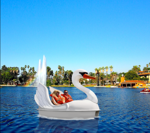 A couple enjoys a swan-shaped paddle boat on a sunny lake with palm trees and a fountain in the background.