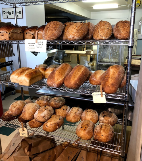 A display of various freshly baked loaves of bread on metal racks in a bakery.