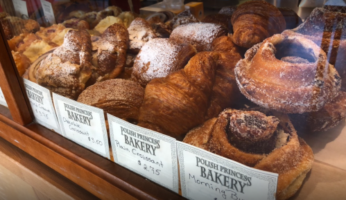 A display case filled with various pastries, including croissants and danishes, labeled with prices from Polish Princess Bakery.