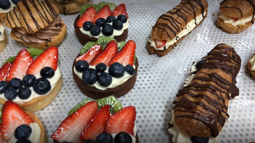 An assortment of desserts featuring fruit-topped pastries, chocolate drizzled treats, and creamy fillings.