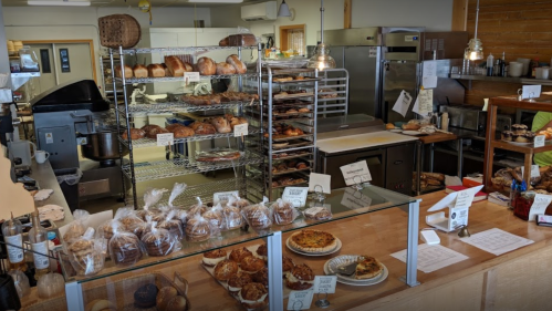 A bakery display with various breads, pastries, and cookies on shelves and counters, showcasing a warm, inviting atmosphere.