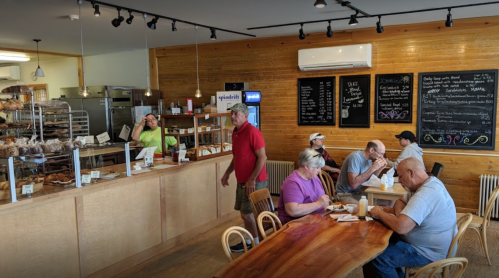 A cozy café interior with customers enjoying food, a counter with baked goods, and a staff member serving.