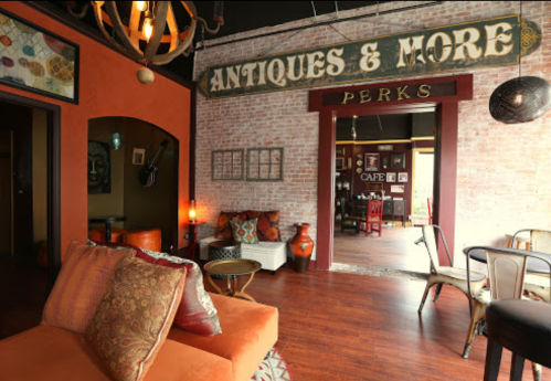 Cozy interior of a vintage shop with orange walls, eclectic decor, and a sign for "Antiques & More" leading to a cafe.