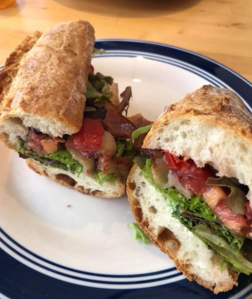 A freshly cut sandwich on a plate, filled with lettuce, tomatoes, and bacon, served on crusty bread.