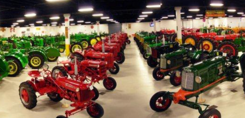A spacious indoor exhibit featuring rows of vintage tractors in various colors, including red and green.