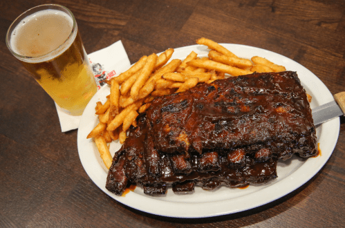 A plate of barbecue ribs with fries and a glass of beer on a wooden table.