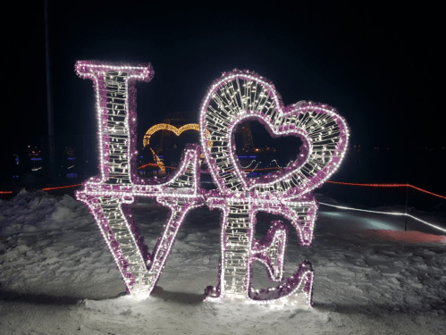 A large illuminated sign spelling "LOVE" with a heart, set against a dark night sky and snowy ground.